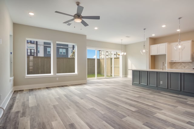 unfurnished living room with sink, ceiling fan with notable chandelier, and light wood-type flooring