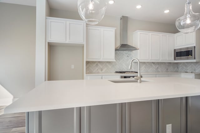 kitchen with white cabinets, stainless steel microwave, an island with sink, and wall chimney range hood