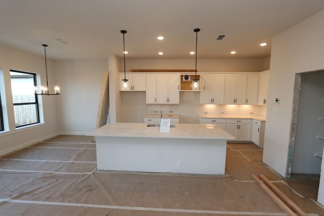 kitchen featuring white cabinets, decorative light fixtures, an inviting chandelier, and a kitchen island with sink