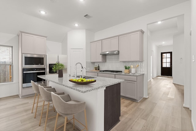 kitchen with stainless steel appliances, sink, vaulted ceiling, a center island with sink, and a breakfast bar area