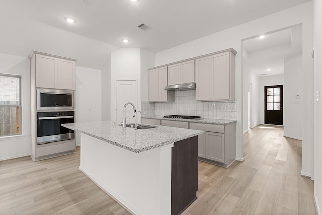 kitchen with sink, light stone counters, a center island with sink, lofted ceiling, and stainless steel appliances