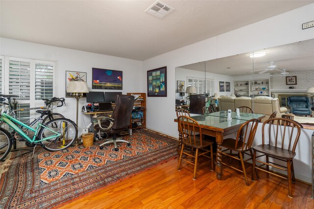 dining space with ceiling fan, hardwood / wood-style floors, and a brick fireplace