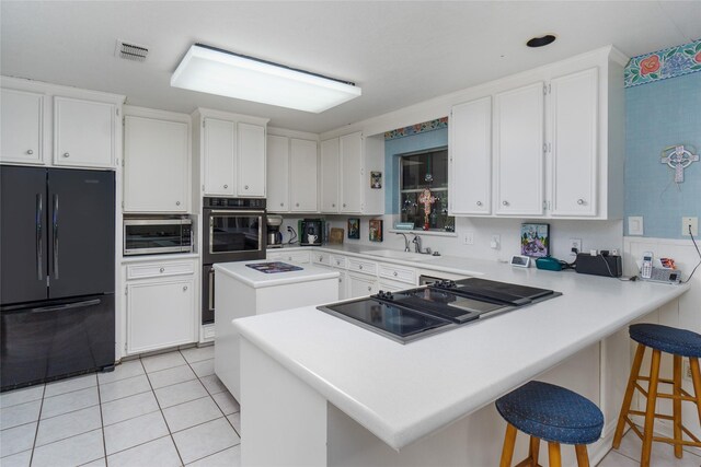 kitchen with black appliances, white cabinetry, light tile patterned floors, and a breakfast bar