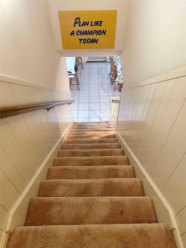 stairs with tile patterned floors and wooden walls