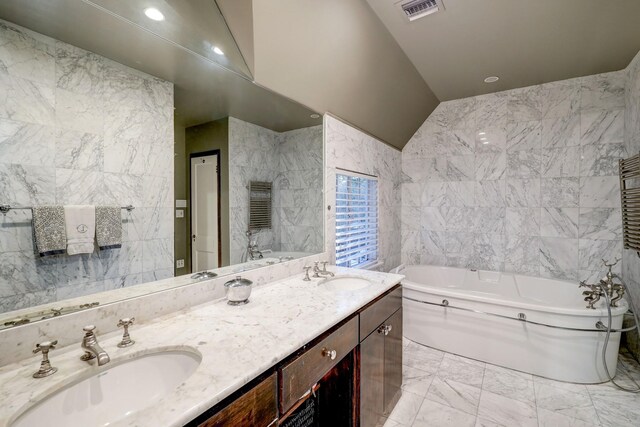 bathroom with tile walls, vaulted ceiling, a tub, and vanity