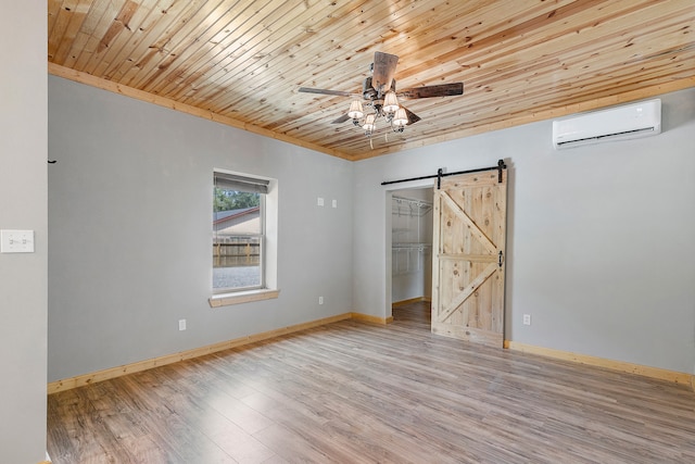 empty room featuring a wall mounted air conditioner, light hardwood / wood-style flooring, ceiling fan, wood ceiling, and a barn door