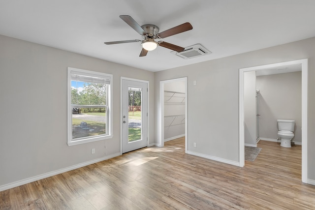 unfurnished bedroom with ensuite bath, light wood-type flooring, a walk in closet, a closet, and ceiling fan