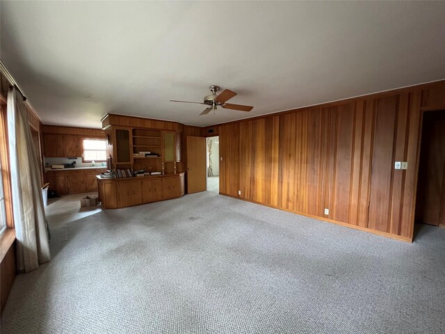 unfurnished living room with light carpet, crown molding, ceiling fan, and wooden walls