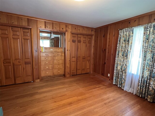 unfurnished bedroom featuring light wood-type flooring, two closets, and wooden walls