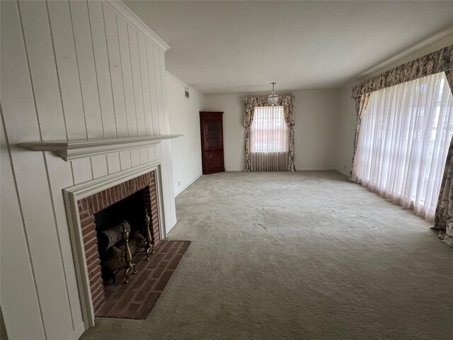 unfurnished living room with a fireplace, ornamental molding, a notable chandelier, and carpet