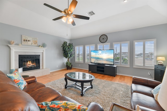 living room with ceiling fan, a tile fireplace, light hardwood / wood-style floors, and vaulted ceiling