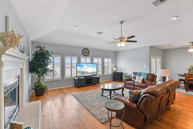 living room with a tile fireplace, ceiling fan, and light wood-type flooring