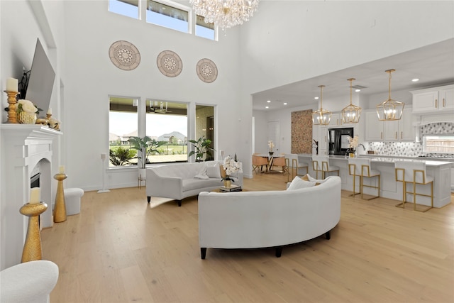 living room with light wood-type flooring, a towering ceiling, an inviting chandelier, and sink