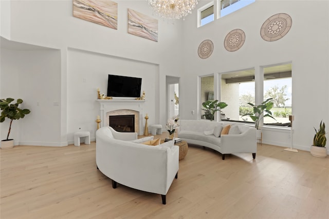 living room featuring a towering ceiling, an inviting chandelier, light wood-type flooring, and a premium fireplace