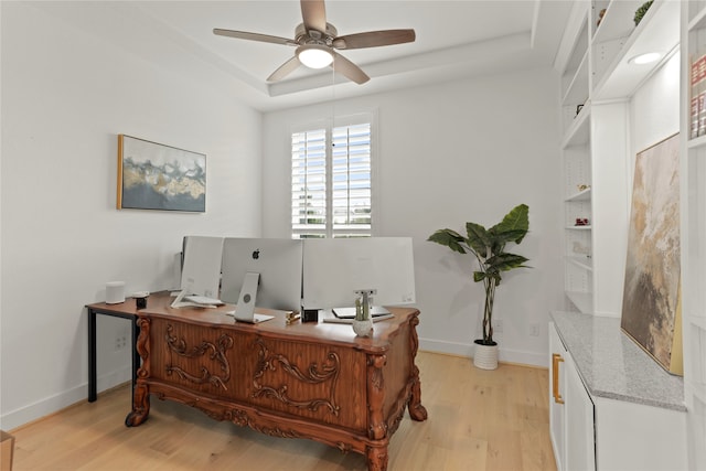 home office with light hardwood / wood-style floors, a tray ceiling, and ceiling fan