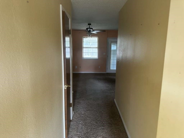 corridor featuring a textured ceiling and dark colored carpet