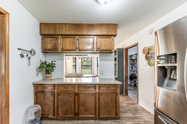 kitchen with stainless steel fridge with ice dispenser, light wood-type flooring, and a textured ceiling