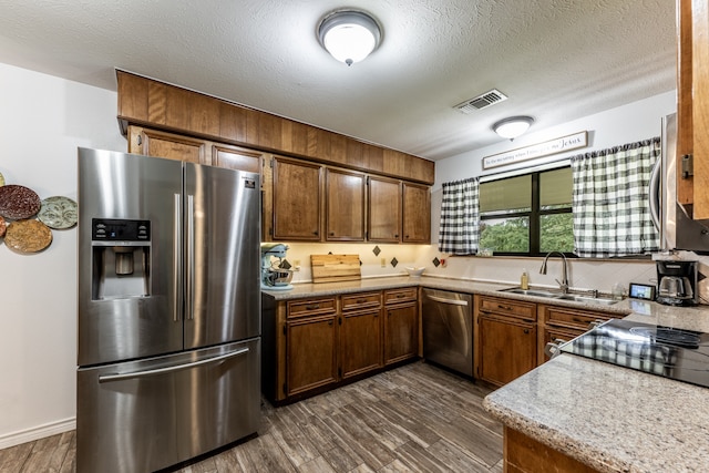 kitchen with a textured ceiling, light stone countertops, dark wood-type flooring, stainless steel appliances, and sink