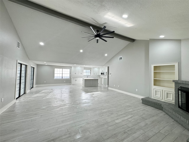 unfurnished living room featuring a fireplace, beamed ceiling, light wood-type flooring, a textured ceiling, and ceiling fan