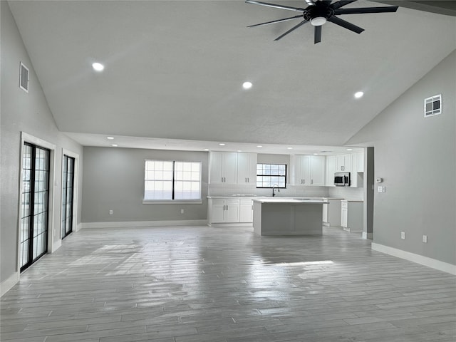 unfurnished living room with ceiling fan, light wood-type flooring, sink, and high vaulted ceiling