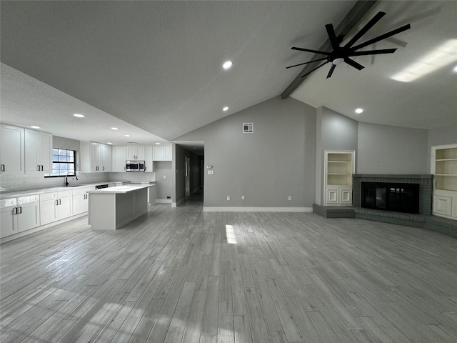 unfurnished living room featuring lofted ceiling with beams, a textured ceiling, light hardwood / wood-style flooring, a brick fireplace, and ceiling fan