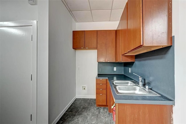 9788 Clarewood Dr Unit 201, Houston, TX 77036 - kitchen with brown cabinetry, a sink, a paneled ceiling, baseboards, and dark tile patterned flooring