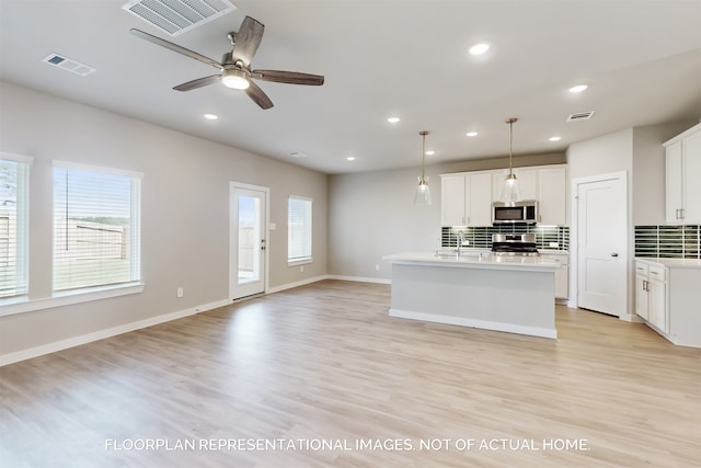 kitchen with decorative light fixtures, white cabinets, a center island with sink, and stainless steel appliances