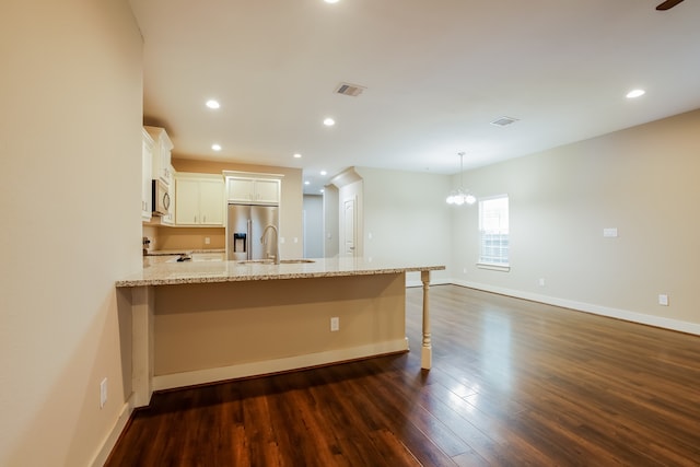 kitchen with white cabinets, appliances with stainless steel finishes, light stone counters, dark hardwood / wood-style floors, and a breakfast bar