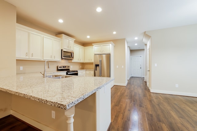 kitchen with dark hardwood / wood-style flooring, appliances with stainless steel finishes, kitchen peninsula, sink, and light stone counters