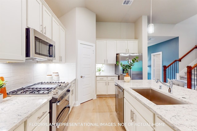 kitchen featuring pendant lighting, stainless steel appliances, decorative backsplash, sink, and light stone counters