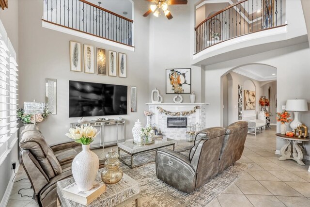 living room featuring light tile patterned floors, ornamental molding, ceiling fan, and a high ceiling