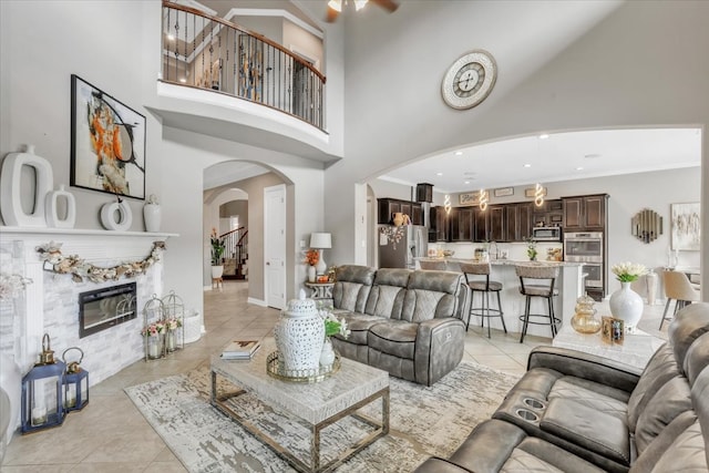 tiled living room with ceiling fan, a towering ceiling, and a premium fireplace