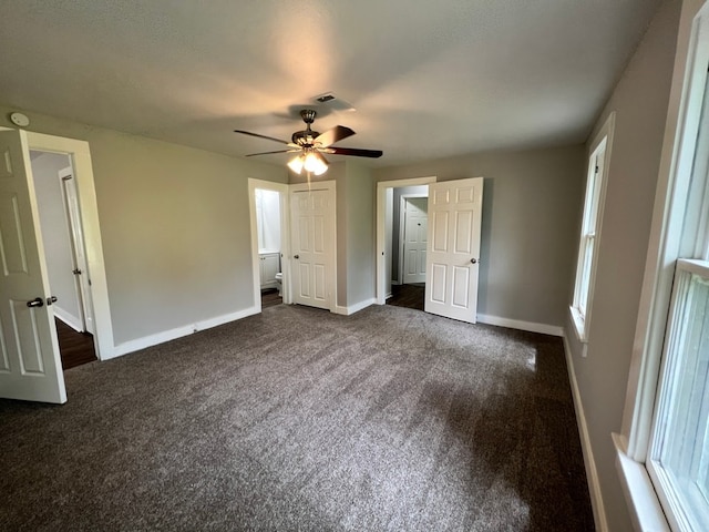 unfurnished bedroom featuring ceiling fan, ensuite bathroom, and dark colored carpet