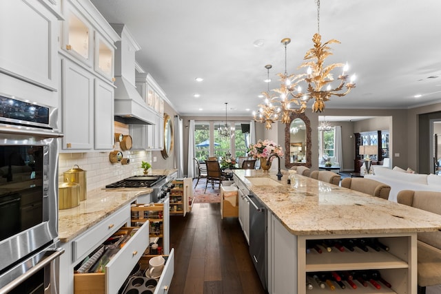 kitchen featuring hanging light fixtures, white cabinetry, dark wood-type flooring, a center island with sink, and a chandelier