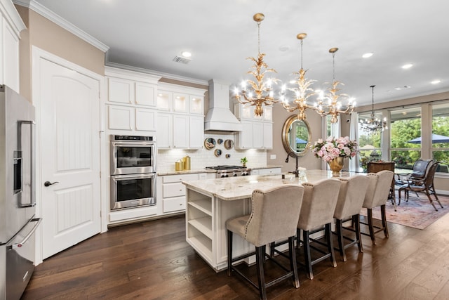 kitchen featuring premium range hood, an island with sink, hanging light fixtures, stainless steel appliances, and a notable chandelier