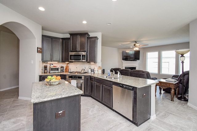kitchen with a ceiling fan, arched walkways, a sink, open floor plan, and stainless steel appliances