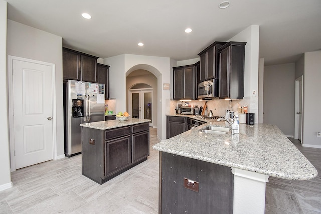 kitchen with dark brown cabinetry, appliances with stainless steel finishes, arched walkways, light stone countertops, and a peninsula