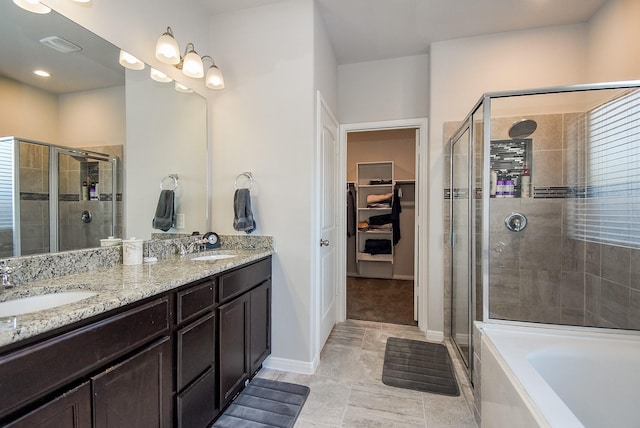 full bath with double vanity, a sink, a walk in closet, and a stall shower