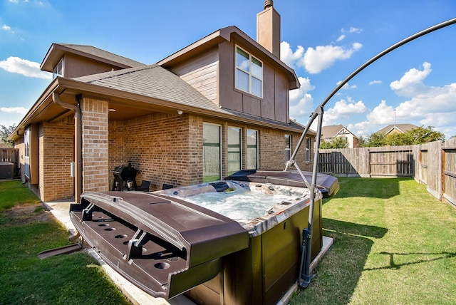 back of property featuring a fenced backyard, a chimney, a hot tub, and brick siding