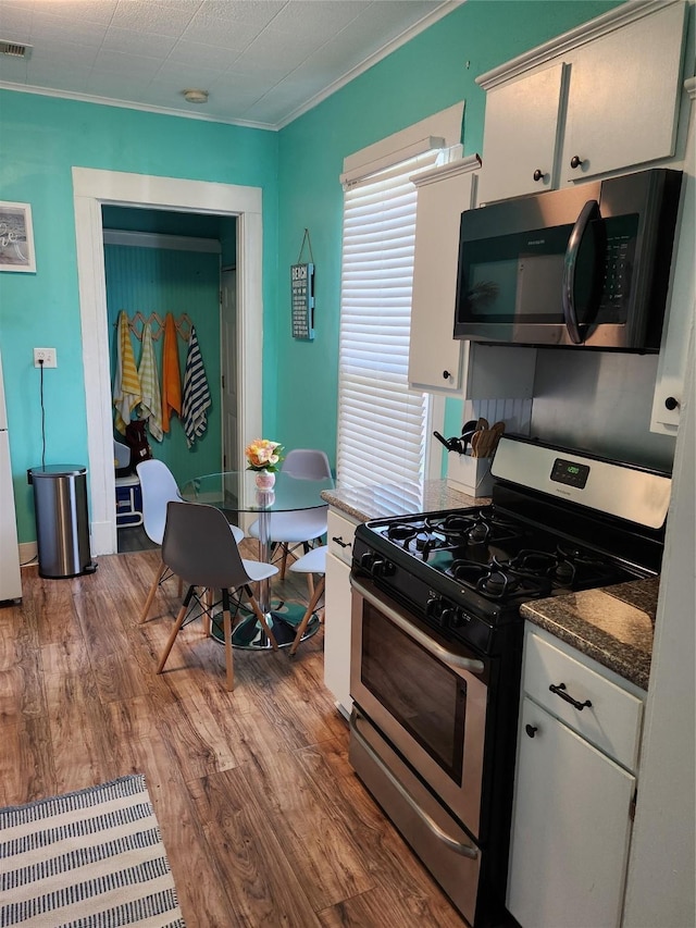 2219 33rd St E, Galveston, TX 77550 - kitchen with dark countertops, appliances with stainless steel finishes, wood finished floors, white cabinets, and ornamental molding