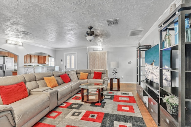 living room with light wood-type flooring, ceiling fan, crown molding, and a textured ceiling