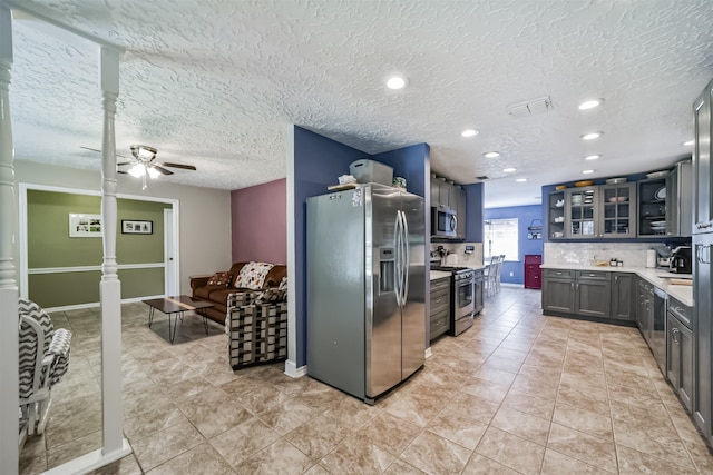 kitchen featuring backsplash, appliances with stainless steel finishes, gray cabinets, ceiling fan, and a textured ceiling