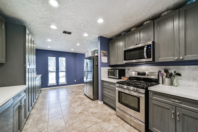 kitchen with light tile patterned floors, a textured ceiling, backsplash, and stainless steel appliances