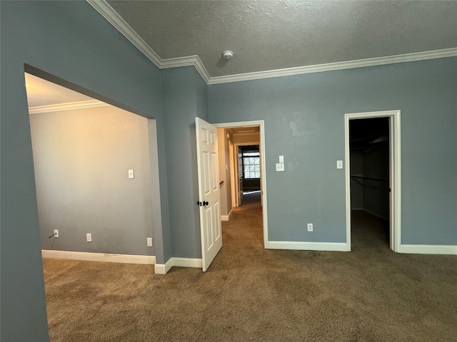 unfurnished bedroom with dark carpet, a walk in closet, crown molding, a textured ceiling, and a closet