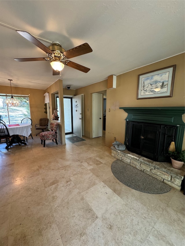 living room featuring a stone fireplace and ceiling fan with notable chandelier