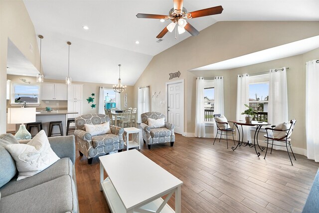 living room with dark wood-type flooring, ceiling fan with notable chandelier, and high vaulted ceiling