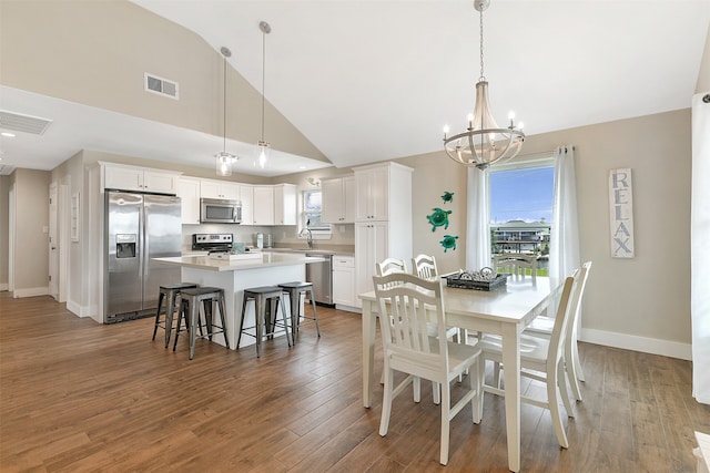 dining space with sink, hardwood / wood-style floors, high vaulted ceiling, and a chandelier