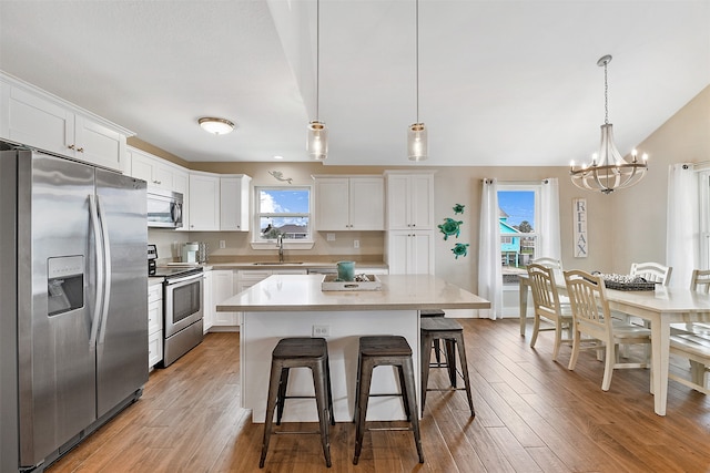 kitchen with appliances with stainless steel finishes, a center island, pendant lighting, and light hardwood / wood-style flooring