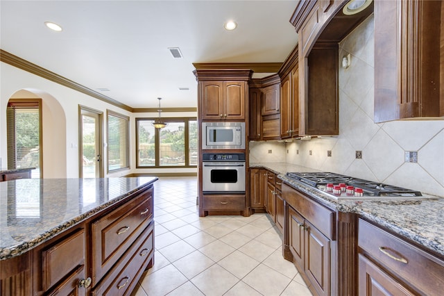 kitchen with appliances with stainless steel finishes, light tile patterned floors, light stone countertops, and ornamental molding