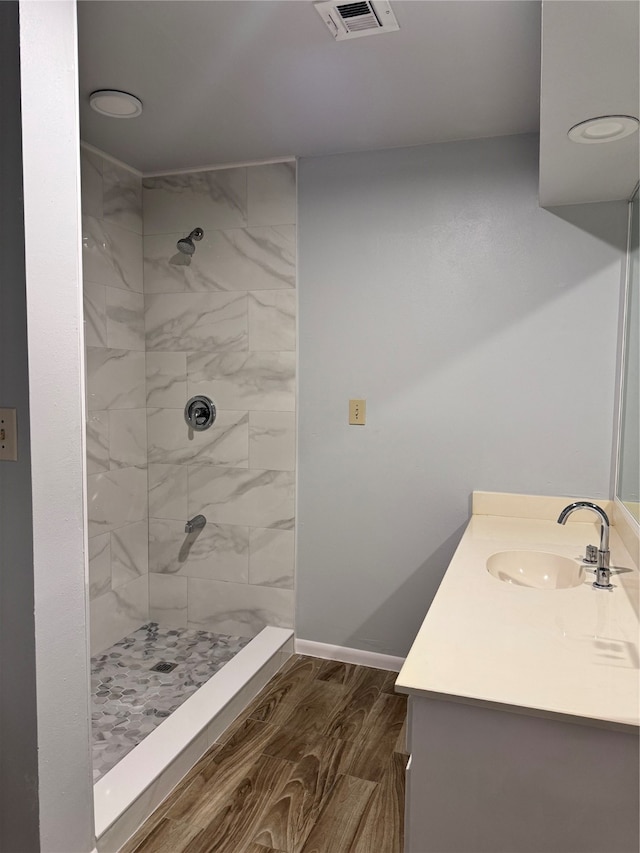 bathroom with wood-type flooring, a tile shower, and vanity